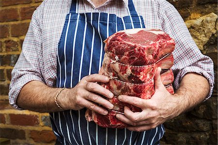 simsearch:6118-08729219,k - Butcher in blue striped apron holding a large piece of beef. Foto de stock - Sin royalties Premium, Código: 6118-08729219