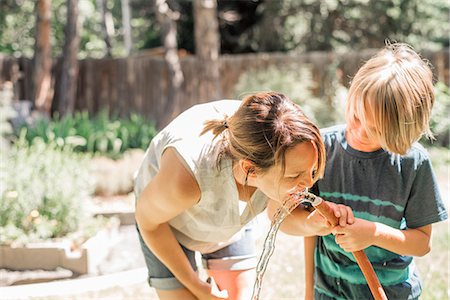 Mother and son standing in a garden, drinking water from a garden hose. Foto de stock - Sin royalties Premium, Código: 6118-08729307