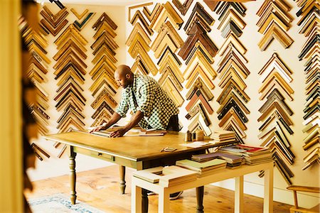 Man working at a picture framers, a large selection of frames on the walls. Foto de stock - Sin royalties Premium, Código: 6118-08729328