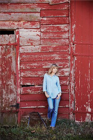 simsearch:6118-08842040,k - A young woman in jeans leaning against a red painted barn building. Stock Photo - Premium Royalty-Free, Code: 6118-08842045