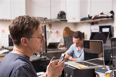 simsearch:6118-08088592,k - Three people working in a technology lab, with a man in the foreground looking at a cellphone. Fotografie stock - Premium Royalty-Free, Codice: 6118-08842007