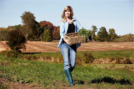 farming woman - A young woman in working clothes walking across a field, holding a basket of crops. Stock Photo - Premium Royalty-Free, Code: 6118-08842025