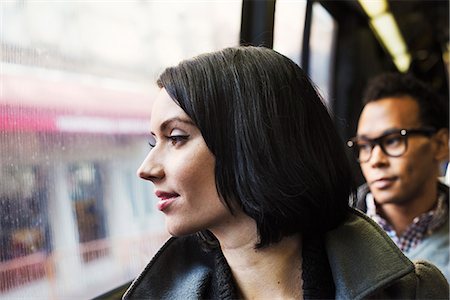 simsearch:6118-08842149,k - A woman sitting on public transport looking out of the window, with a young man in the background. Foto de stock - Royalty Free Premium, Número: 6118-08842146