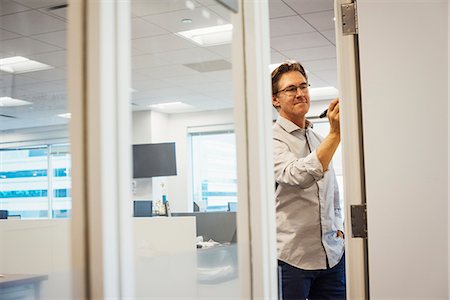 simsearch:6118-09079486,k - A man standing in an office writing on a whiteboard, seen through a doorway. Foto de stock - Royalty Free Premium, Número: 6118-08842125