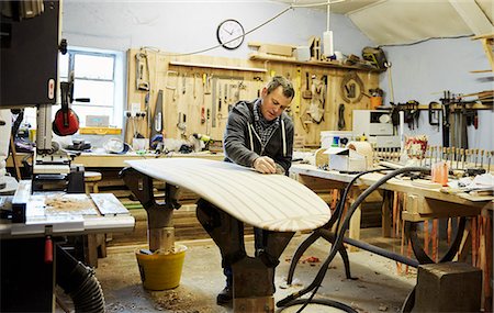 Man standing in a workshop sanding and shaping a wooden surfboard. Fotografie stock - Premium Royalty-Free, Codice: 6118-08860581