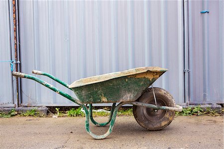 Green wheelbarrow on a building site in front of a metal container. Photographie de stock - Premium Libres de Droits, Code: 6118-08947493