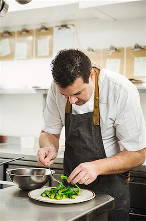 simsearch:6118-08947561,k - Chef standing in the kitchen in a small hotel, plating up a dish of vegetables. Foto de stock - Royalty Free Premium, Número: 6118-08947544