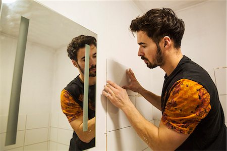 A builder, tiler placing tiles on a wall next to a mirror. Fotografie stock - Premium Royalty-Free, Codice: 6118-08947508