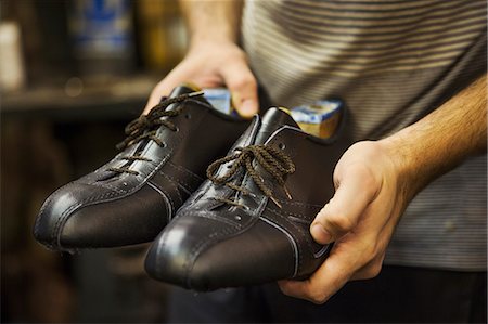 simsearch:6118-08947633,k - Close up of man standing in a shoemaker's workshop, holding a pair of handmade leather lace up cycling shoes. Photographie de stock - Premium Libres de Droits, Code: 6118-08947629