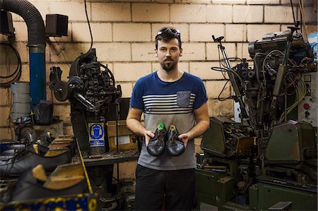 simsearch:6118-08947633,k - Man standing in a shoemaker's workshop, holding a pair of brown leather laced cycling shoes. Photographie de stock - Premium Libres de Droits, Code: 6118-08947631