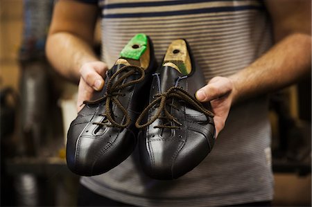simsearch:6118-08947633,k - Close up of man standing in a shoemaker's workshop, holding a pair of handmade cycling shoes. Photographie de stock - Premium Libres de Droits, Code: 6118-08947632