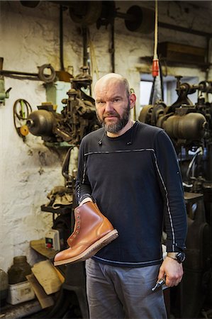 simsearch:6118-08947633,k - Man standing in a shoemaker's workshop, holding a pair of brown leather ankle boots. Photographie de stock - Premium Libres de Droits, Code: 6118-08947634