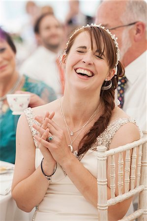 simsearch:6118-08947762,k - Bride in her wedding dress sitting in a marquee, hands clasped and laughing. Stockbilder - Premium RF Lizenzfrei, Bildnummer: 6118-08947763