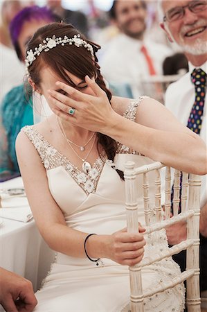 simsearch:6118-08947762,k - Bride in her wedding dress sitting in a marquee, laughing and covering her face. Stockbilder - Premium RF Lizenzfrei, Bildnummer: 6118-08947764