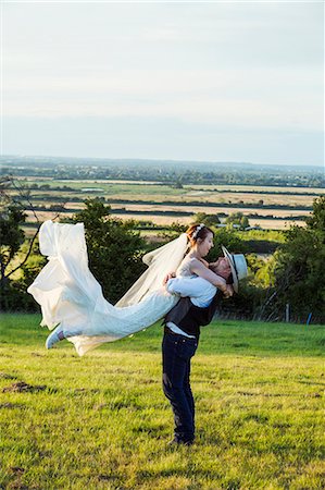 simsearch:6118-08947762,k - Newlyweds standing in a grass meadow overlooking a rural view, groom hugging and swinging the bride in the air. Stockbilder - Premium RF Lizenzfrei, Bildnummer: 6118-08947793
