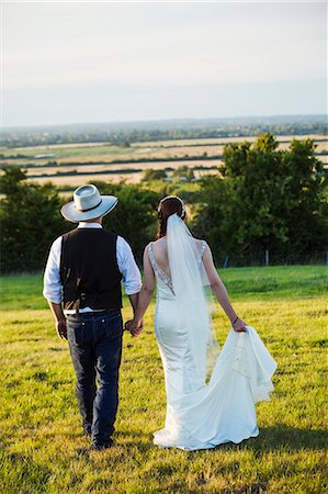simsearch:6118-08947762,k - Rear view of bride and groom walking hand in hand across a grassy slope, with a view over the landscape. Stockbilder - Premium RF Lizenzfrei, Bildnummer: 6118-08947792