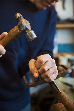 forger - Man standing in a workshop, holding a hammer and wood chisel, working on a piece of wood. Photographie de stock - Premium Libres de Droits, Code: 6118-08947794