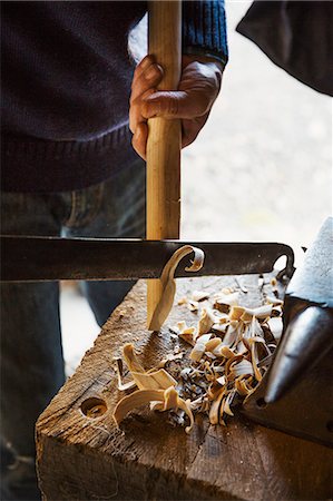 A man in a workshop, holding a tool, cutting and shaping a piece of wood. Stock Photo - Premium Royalty-Free, Code: 6118-08947795