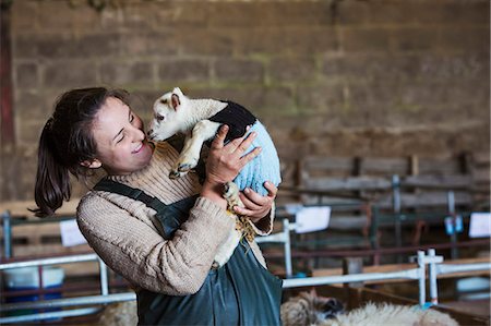 Woman standing in a barn, holding a newborn lamb dressed in a knitted jumper. Stock Photo - Premium Royalty-Free, Code: 6118-08947733