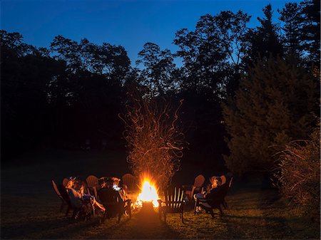 People seated around a campfire in the gathering darkness. Photographie de stock - Premium Libres de Droits, Code: 6118-08947854
