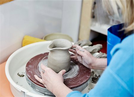A woman using a pottery wheel, placing a small moulded thrown object, a jug with a handle in the centre of the wheel circle. Stock Photo - Premium Royalty-Free, Code: 6118-08947819