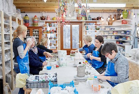 simsearch:6118-08660001,k - A group of people seated at a workbench in a pottery workshop, handbuilding clay objects. A woman with a cup of tea. Stock Photo - Premium Royalty-Free, Code: 6118-08947835