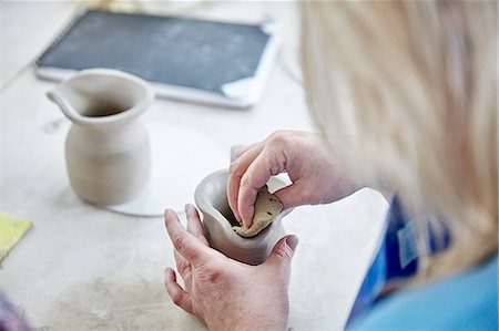 A woman using her hands to shape and smooth a wet clay jug to match another, making a pair. Stock Photo - Premium Royalty-Free, Code: 6118-08947839