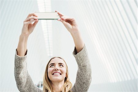 A young woman taking a photograph with her phone, a selfie in the World Trade Centre Oculus building with a stunning white ribbed arched roof. Stock Photo - Premium Royalty-Free, Code: 6118-08971294