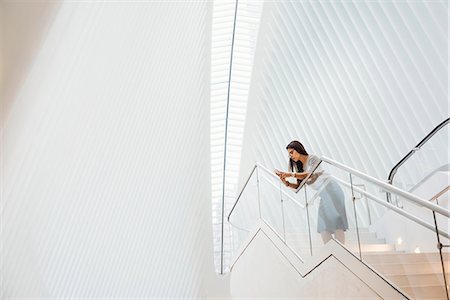 distant city - A woman on the stairs leaning on a railing in the vast space of the atrium of the Oculus building at the World Trade Centre site in New York City. Stock Photo - Premium Royalty-Free, Code: 6118-08971298