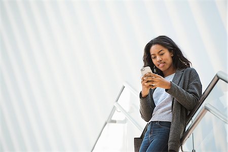 A woman standing on a stairway in the Oculus building at the World Trade Centre under a dramatic ridged white ceiling, checking her phone. Stock Photo - Premium Royalty-Free, Code: 6118-08971303