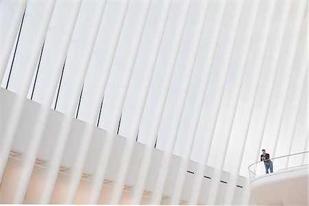 A person standing alone in an atrium by a railing, in the Oculus building under a high white ridged ceiling. Stock Photo - Premium Royalty-Free, Code: 6118-08971300