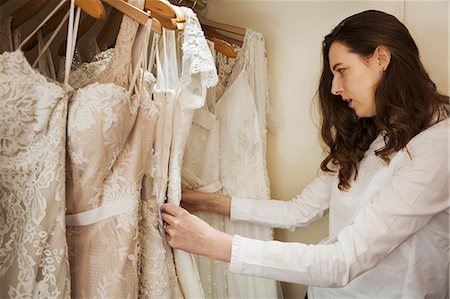 simsearch:6118-08971470,k - A young woman with long brown hair looking through the rails of wedding dresses in a shop. Choosing. Photographie de stock - Premium Libres de Droits, Code: 6118-08971446