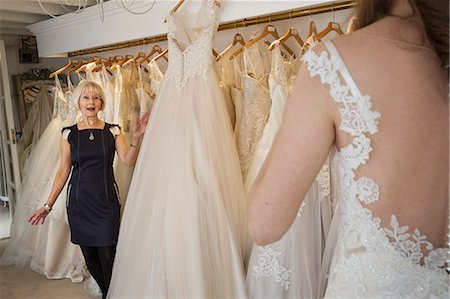 simsearch:6118-08971470,k - A woman, a bride to be, trying on dresses with the help of a sales assistant, in a wedding dress shop. Photographie de stock - Premium Libres de Droits, Code: 6118-08971455