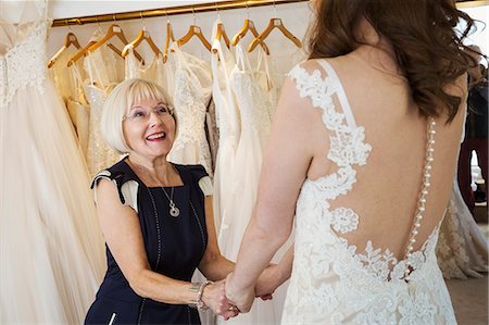 simsearch:6118-08971470,k - A woman, a bride to be, trying on dresses with the help of a sales assistant, in a wedding dress shop. Photographie de stock - Premium Libres de Droits, Code: 6118-08971456
