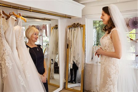 simsearch:6118-08971470,k - A woman, a bride to be, trying on dresses with the help of a sales assistant, in a wedding dress shop. Photographie de stock - Premium Libres de Droits, Code: 6118-08971458
