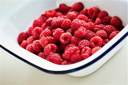 simsearch:6102-08559167,k - Close up high angle view of fresh raspberries in white enamel dish with blue rim. Foto de stock - Royalty Free Premium, Número: 6118-08971475