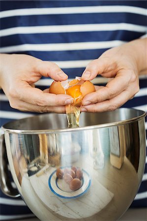 simsearch:6118-08971487,k - Close up of person wearing a blue and white stripy apron separating egg over a metal bowl. Stockbilder - Premium RF Lizenzfrei, Bildnummer: 6118-08971487