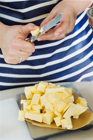 simsearch:6118-08023760,k - Close up of person wearing a blue and white stripy apron holding a knife, cutting butter into small pieces. Stock Photo - Premium Royalty-Free, Code: 6118-08971484