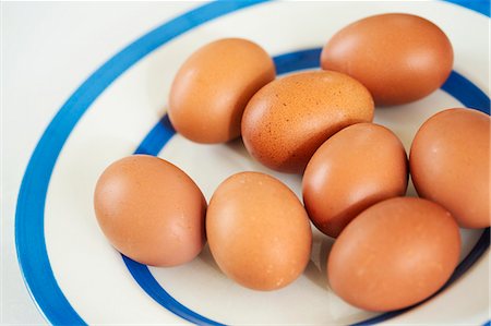 simsearch:6118-08971487,k - Close up high angle view of fresh brown eggs on a white plate with blue stripes. Stockbilder - Premium RF Lizenzfrei, Bildnummer: 6118-08971486