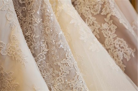 simsearch:6118-08971470,k - Rows of wedding dresses on display in a specialist wedding dress shop. Close up of full skirts, some with a lace overlay, in a variety of colour tones. Photographie de stock - Premium Libres de Droits, Code: 6118-08971419