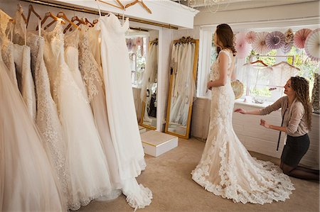 simsearch:6118-08971470,k - Rows of wedding dresses on display. A young woman in a full length white wedding dress, looking at her reflection in the mirror in a bridal boutique. Photographie de stock - Premium Libres de Droits, Code: 6118-08971424