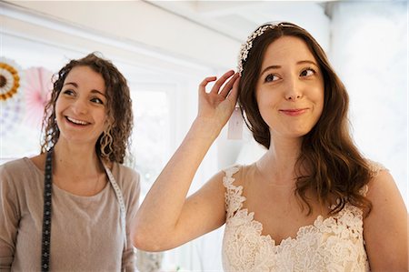 simsearch:6118-08971470,k - A young woman trying on hair accessories, and veil with a white lace overlay wedding dress, assisted by a retail advisor. Photographie de stock - Premium Libres de Droits, Code: 6118-08971429