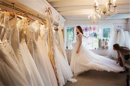 simsearch:6118-08971470,k - Rows of wedding dresses on display in a specialist wedding dress shop. A young woman trying on a wedding dress with a long train. Photographie de stock - Premium Libres de Droits, Code: 6118-08971433