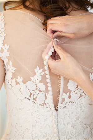 simsearch:6118-08971470,k - Hands doing up the small buttons on the back of a wedding dress with a net bodice and lace detail.  A bride getting ready. Photographie de stock - Premium Libres de Droits, Code: 6118-08971432