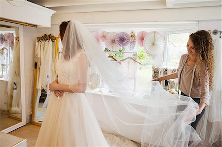 formal gown on clothes hanger - A young woman in a full length white wedding dress, and an assistant or dressmaker holding out her long net veil. Stock Photo - Premium Royalty-Free, Code: 6118-08971437