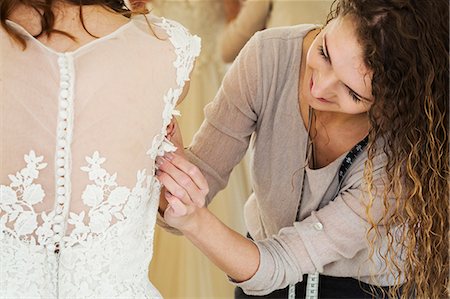 formal gown on clothes hanger - A young woman in a white wedding dress, and a dressmaker fitting the bodice and waist, adjusting the sizing. Stock Photo - Premium Royalty-Free, Code: 6118-08971435