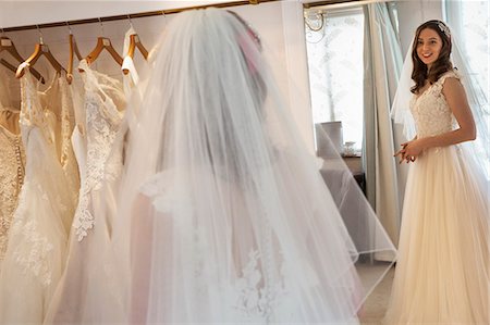 simsearch:6118-08971470,k - A young woman in a full length white wedding dress, looking at her reflection in the mirror in a bridal boutique. Photographie de stock - Premium Libres de Droits, Code: 6118-08971438
