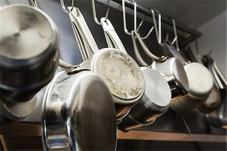 simsearch:6118-08971609,k - Close up of stainless steel pots and pans hanging on metal hooks on a shelf in a restaurant kitchen. Foto de stock - Royalty Free Premium, Número: 6118-08971563