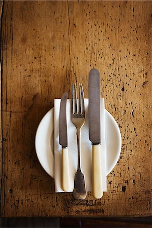 simsearch:6118-08971530,k - Close up high angle view of plate with knives and fork and a serviette on a rustic wooden table. Foto de stock - Sin royalties Premium, Código: 6118-08971577