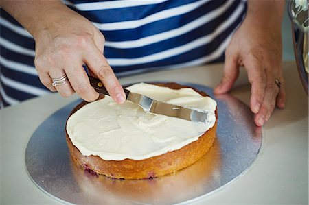Close up high angle view of person wearing a blue and white stripy apron spreading cream over the top of a cake. Stockbilder - Premium RF Lizenzfrei, Bildnummer: 6118-08971501